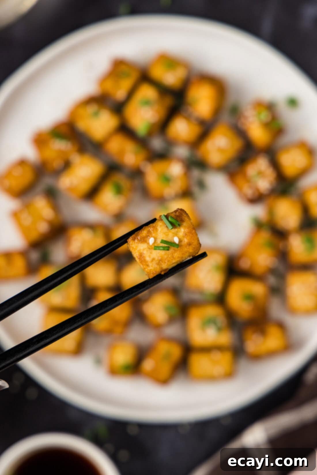 Crispy Golden Tofu 11 Chopsticks delicately holding up a single piece of perfectly golden and exceptionally crispy deep-fried tofu, showcasing its inviting texture and delicious appearance.