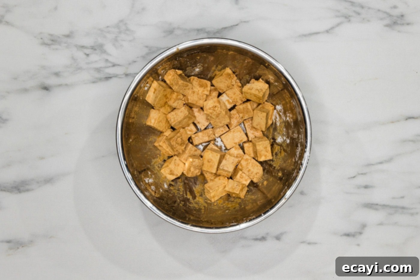 Crispy Golden Tofu 8 Tofu cubes in a mixing bowl, now thoroughly coated with both the savory seasonings and a light, even dusting of cornstarch, primed for deep frying.