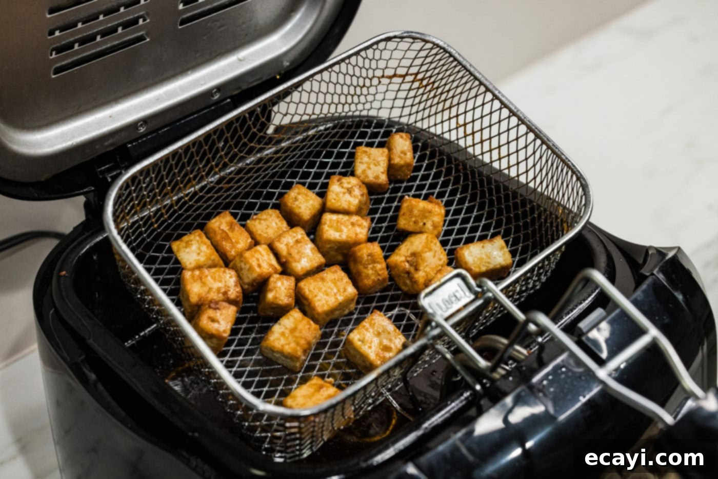 Crispy Golden Tofu 10 Freshly deep-fried tofu cubes being carefully lifted from the fryer basket, showcasing their perfectly golden and crispy exterior, ready to be transferred for draining.