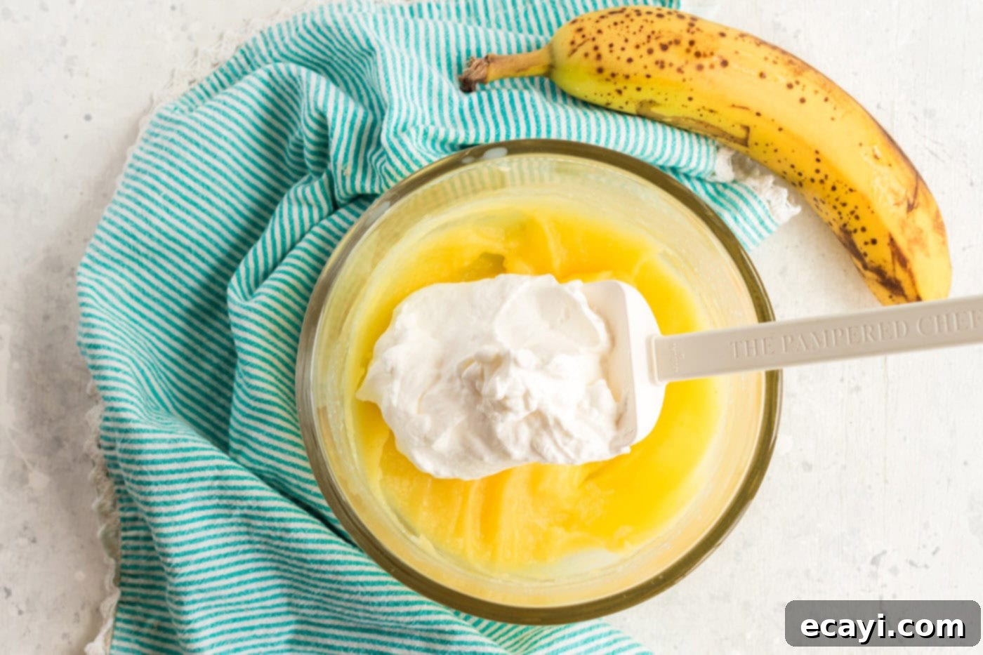 Effortless Banana Cake 9 whipped cream being folded into the banana pudding mixture in a bowl