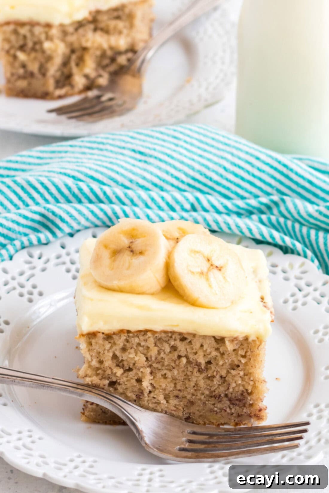 This banana cake using cake mix is positively delicious, easy to make and is topped with an amazing banana flavored whipped cream frosting! slice of banana cake with frosting on a white plate