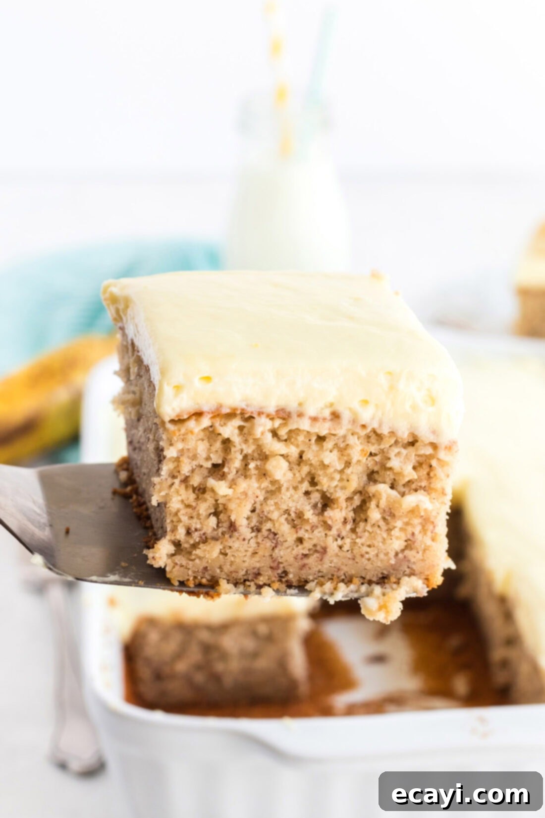 This banana cake using cake mix is positively delicious, easy to make and is topped with an amazing banana flavored whipped cream frosting! spatula holding a slice of banana cake with frosting