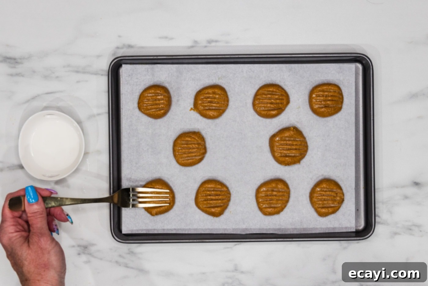Guilt-Free Keto Peanut Butter Treats 7 fork pressing into peanut butter cookie dough on a baking sheet, creating the classic crisscross pattern
