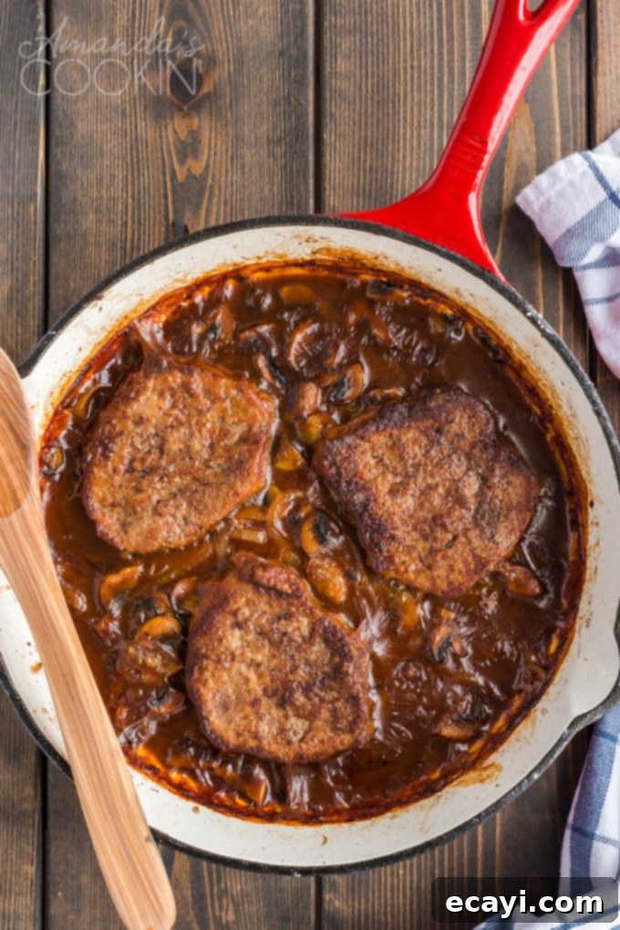 This oven Swiss steak is a delicious twist on a vintage classic. It uses fresh mushrooms and plenty of beef broth for flavor. A comforting, updated recipe! Freshly baked oven Swiss steak with savory gravy in a cast iron skillet