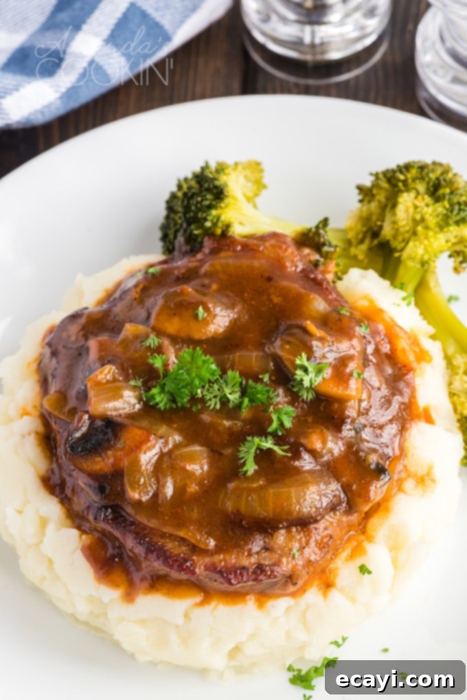 This oven Swiss steak is a delicious twist on a vintage classic. It uses fresh mushrooms and plenty of beef broth for flavor. A comforting, updated recipe! Oven Swiss steak covered in gravy, served on a bed of mashed potatoes