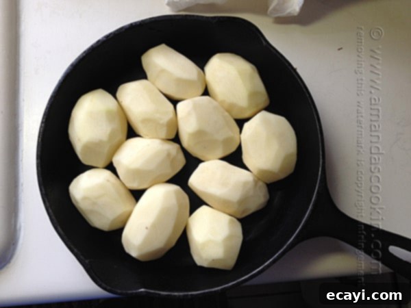 Crispy Cast Iron Roast Potatoes 5 Peeled russet potatoes carefully arranged in a cast iron skillet, ready for the addition of broth and seasoning.