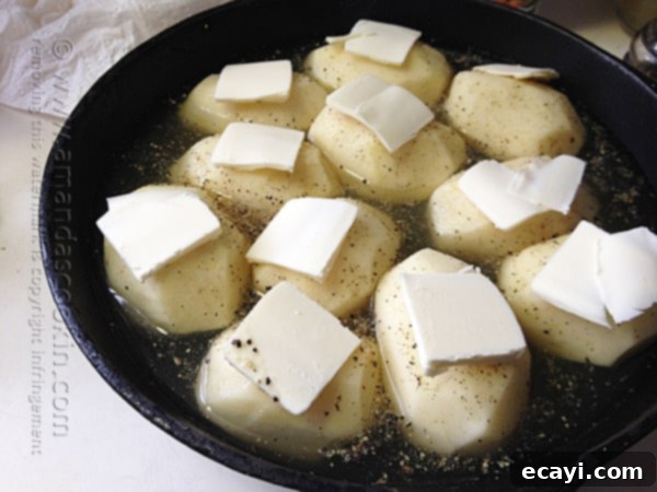 Crispy Cast Iron Roast Potatoes 7 Close-up of seasoned and butter-topped peeled potatoes in a cast iron skillet, awaiting their transformation in the oven.