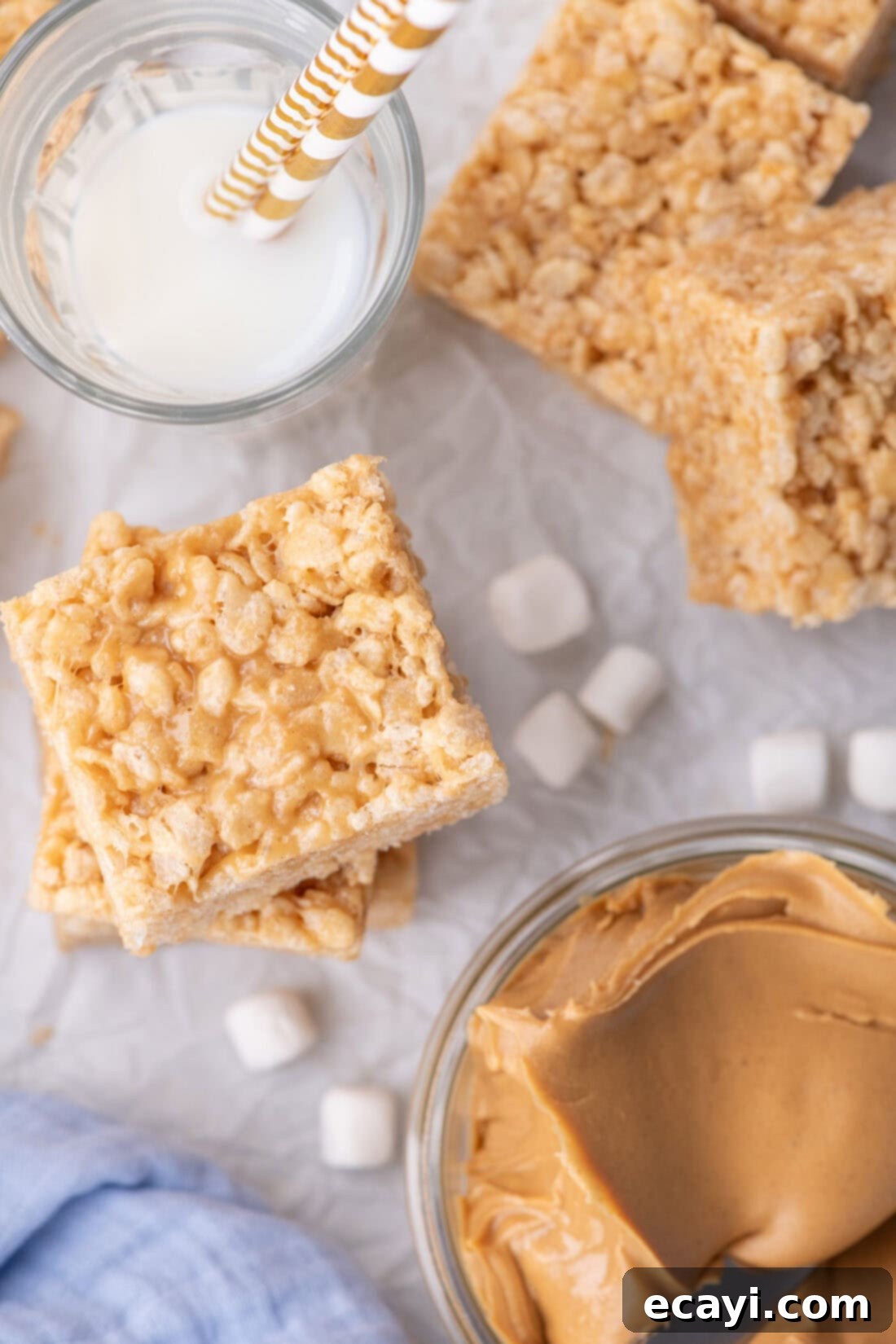 Crunchy Peanut Butter Krispie Delights 11 Stacked Peanut Butter Rice Krispie Treats beside a bowl of creamy peanut butter and a refreshing glass of milk, ready for a delicious snack.