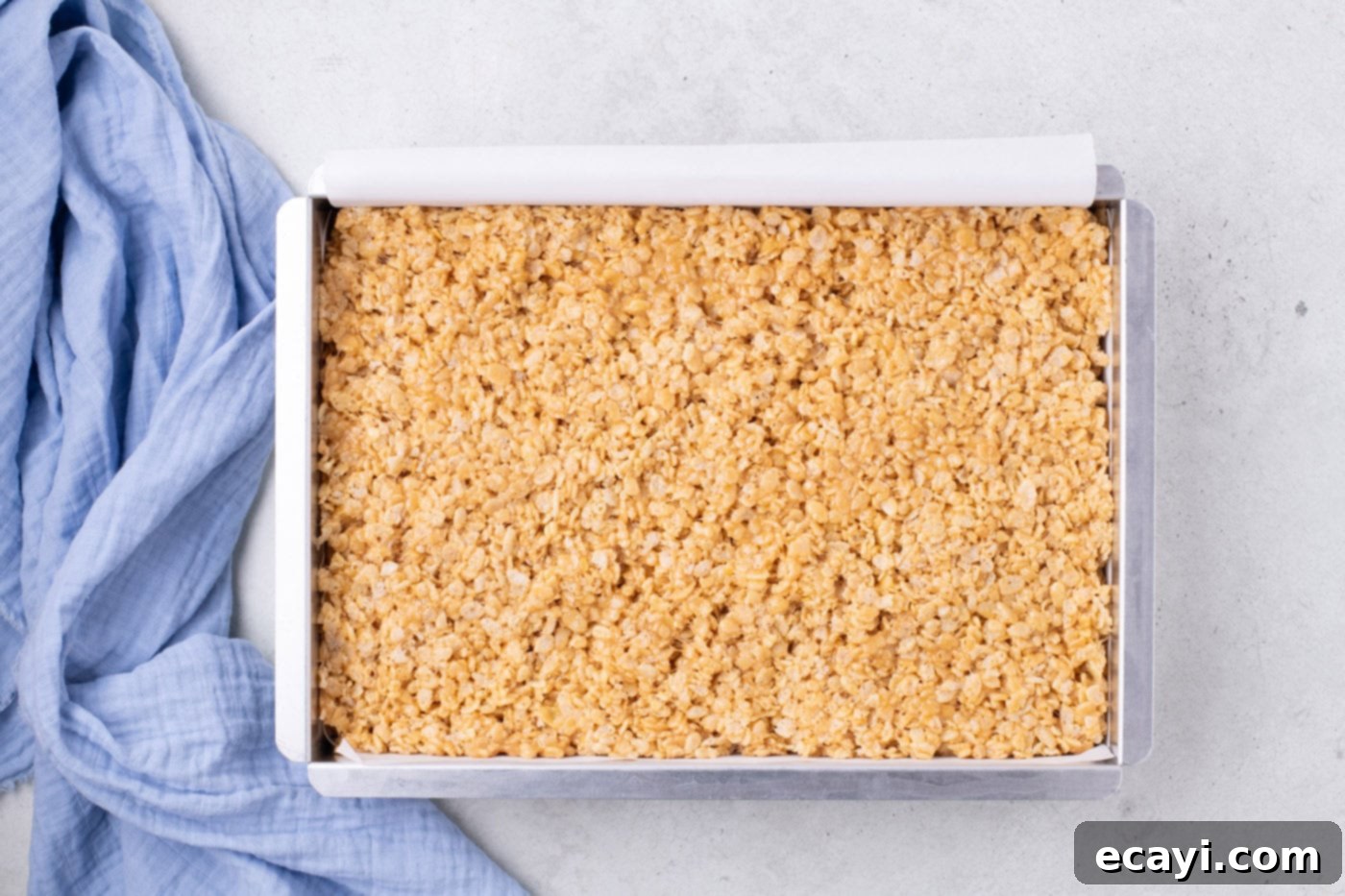 Crunchy Peanut Butter Krispie Delights 9 The peanut butter Rice Krispies mixture being pressed evenly into a parchment-lined baking pan.