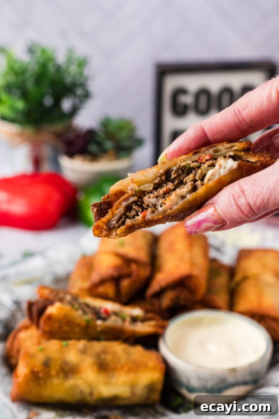 Crispy Philly Cheesesteak Rolls 16 Hand holding up a Philly Cheesesteak Egg Roll cut in half