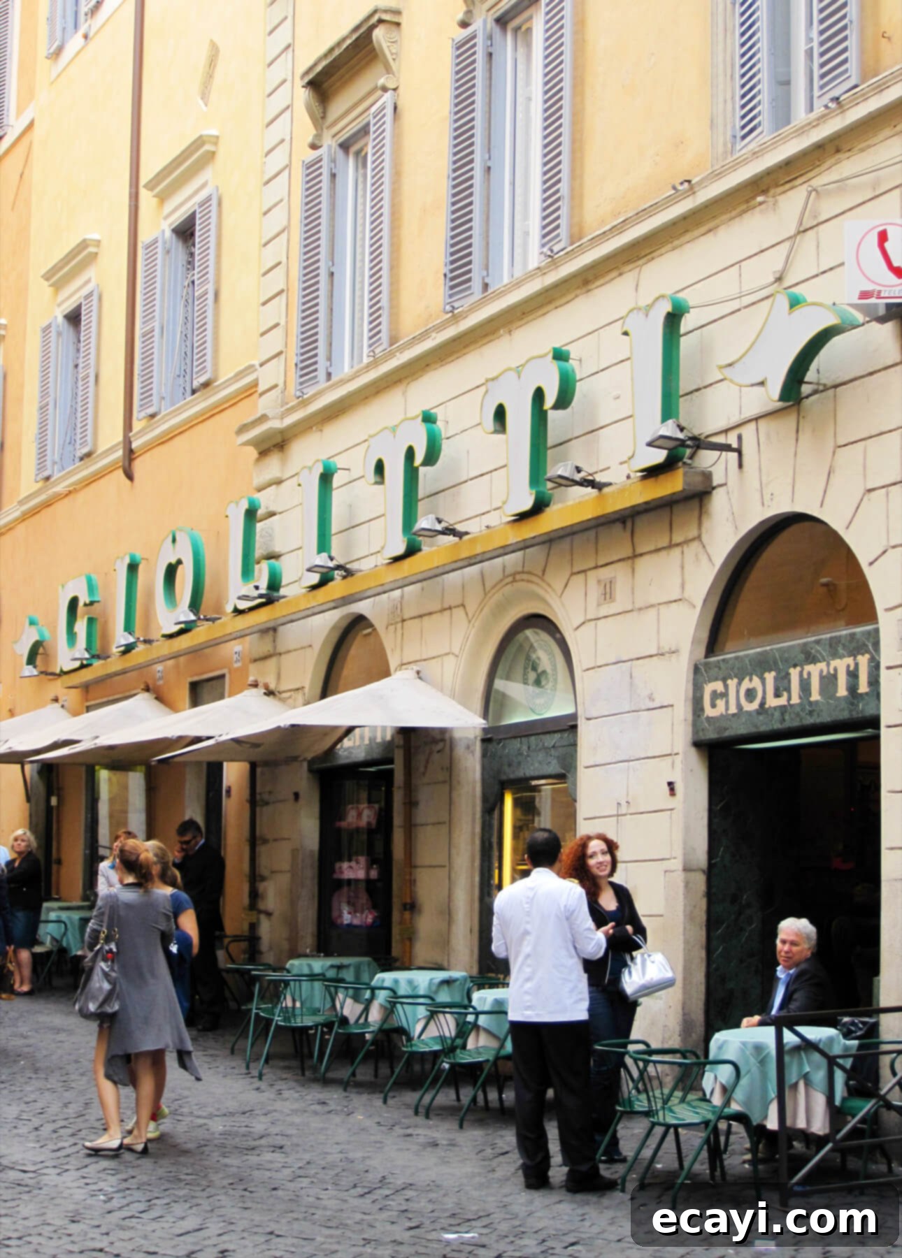 Velvet Blueberry Gelato 3 People gather outside Giolitti, a gelato shop in Rome with green signage in a historic building. Umbrellas and tables line the cobblestone street as customers savor gelato. Classic architecture and wooden shutters add to the charming atmosphere. // FoodNouveau.com