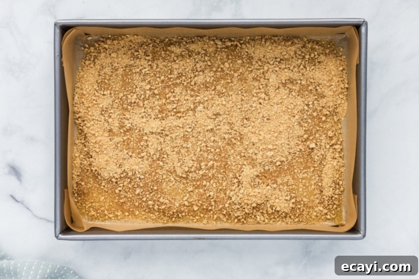 Pure Magic Dessert Bars 6 Graham cracker crumbs uniformly sprinkled over melted butter in a baking pan.