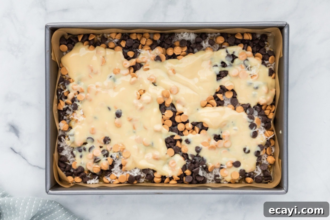 Pure Magic Dessert Bars 9 Sweetened condensed milk being poured slowly and evenly over the chocolate chip layer in the baking pan.