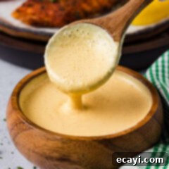 Classic Remoulade 8 Close up photo of a spoon drizzling Remoulade Sauce into a bowl, showcasing its rich texture.