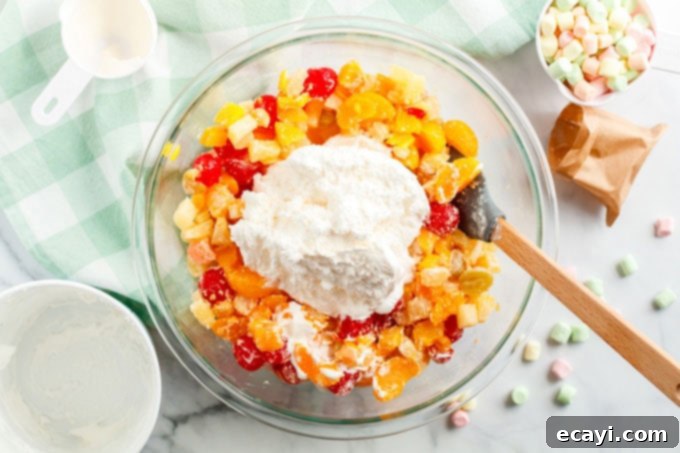 Heavenly Ambrosia Fruit Delight 6 Cool Whip and sour cream being added over the fruit and pudding mixture in a large bowl.