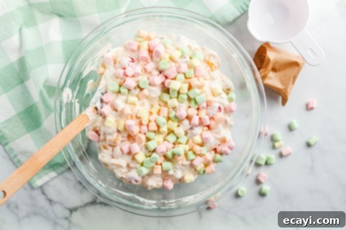 Heavenly Ambrosia Fruit Delight 7 Colorful miniature marshmallows being folded into the Ambrosia Salad mixture, adding fluffiness.