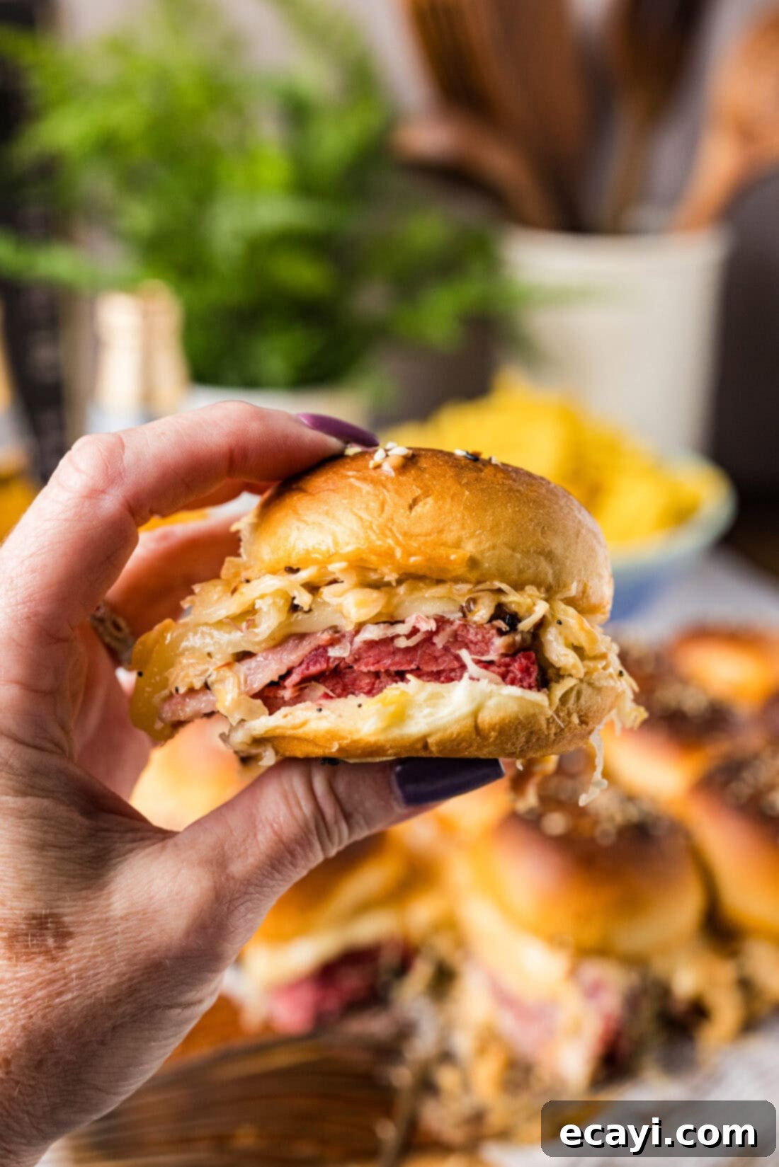 Reuben Bites 3 A hand reaching for a perfectly golden-brown Reuben Slider from a platter.