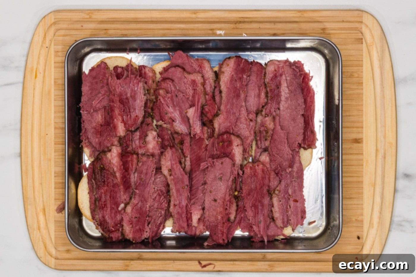 Reuben Bites 5 Sliced corned beef arranged on the bottom halves of slider buns in a baking dish.