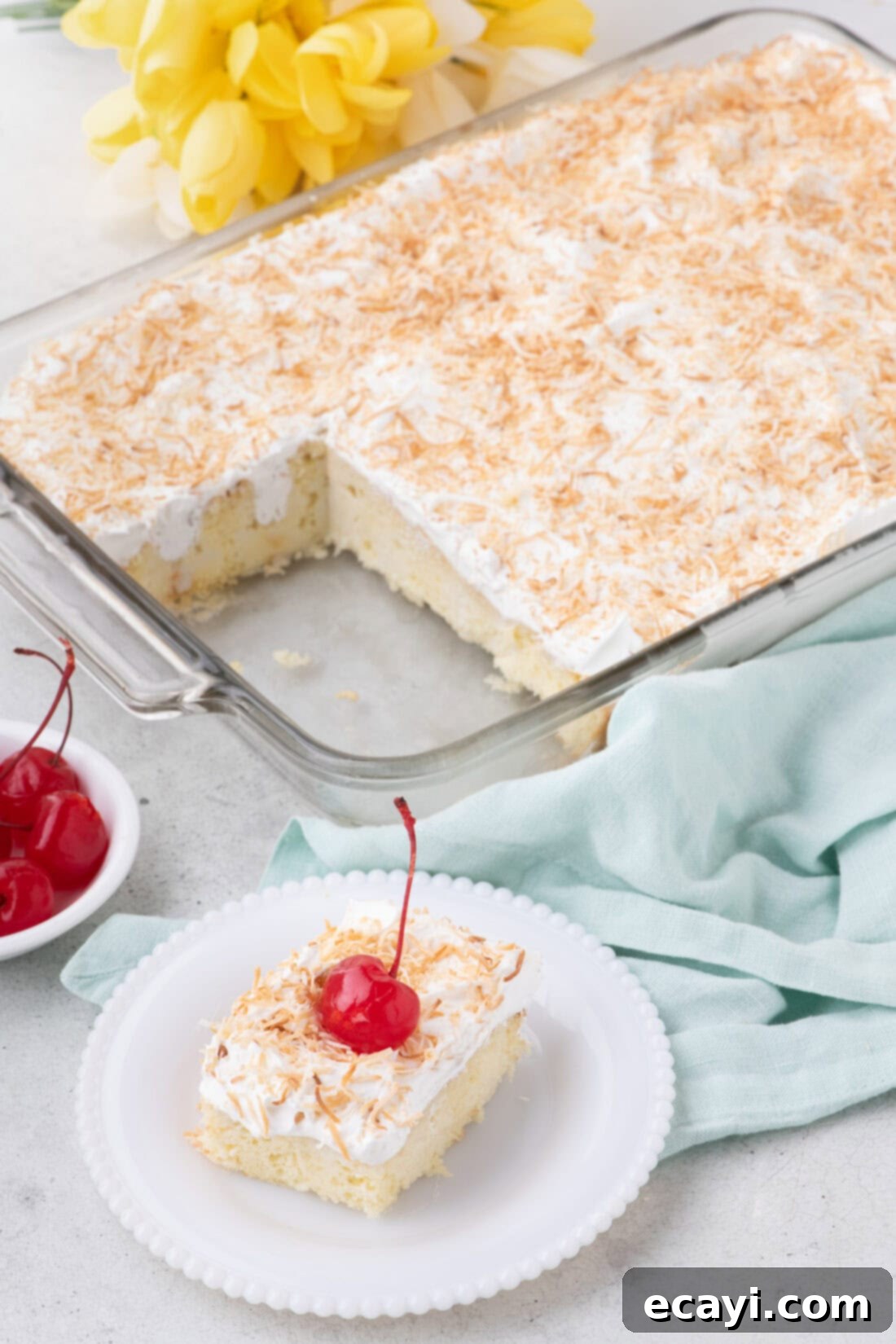 Tropical Coconut Infusion Cake 11 A large Coconut Poke Cake in a baking dish with a slice cut out and placed on a plate in the foreground.