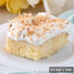 Tropical Coconut Infusion Cake 12 Close up photo of a slice of Coconut Poke Cake, showing the layers of cake, filling, and whipped topping with toasted coconut.