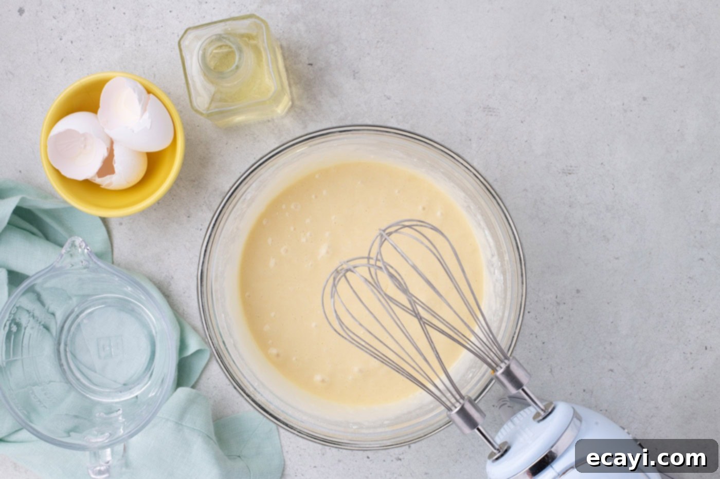 Tropical Coconut Infusion Cake 5 Cake batter being mixed in a bowl with a hand mixer, showing a smooth consistency.