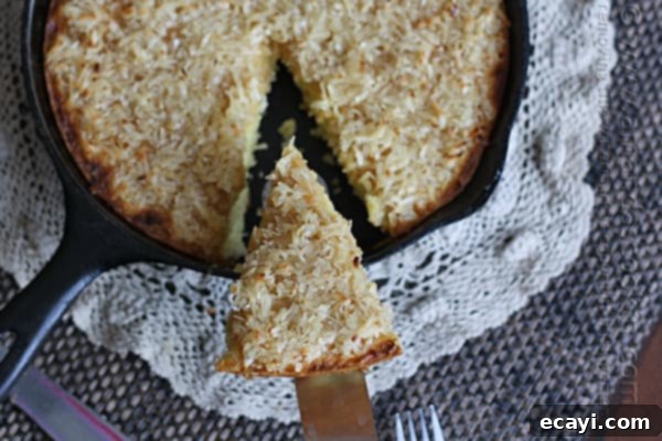 Effortless Golden Coconut Cake 3 An overhead photo of a golden Lazy Daisy Cake in a cast iron skillet, with a slice being removed.