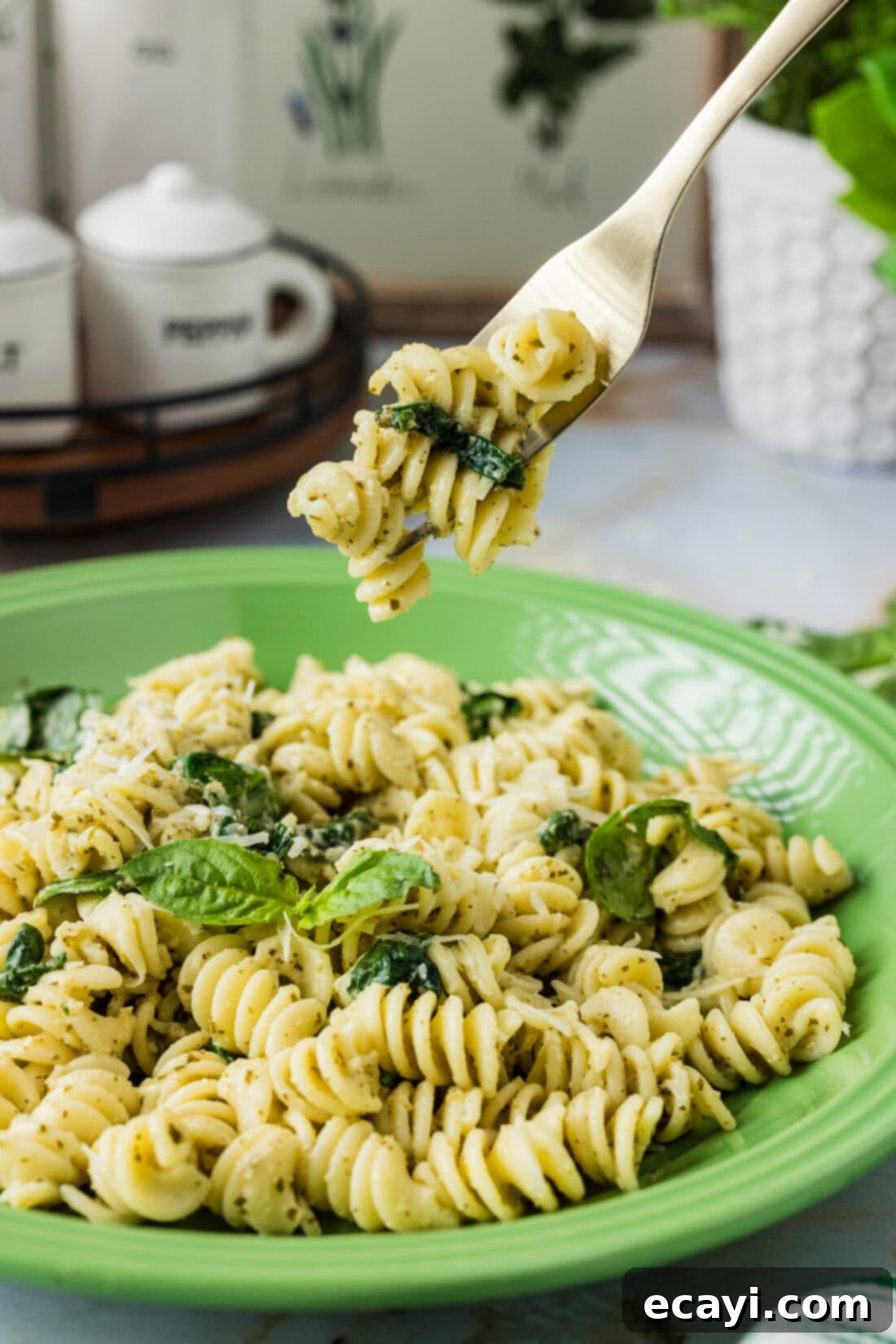 Pesto Perfection 3 Forkful of Pesto Pasta held above a plate of Pesto Pasta, showcasing the creamy texture and fresh spinach