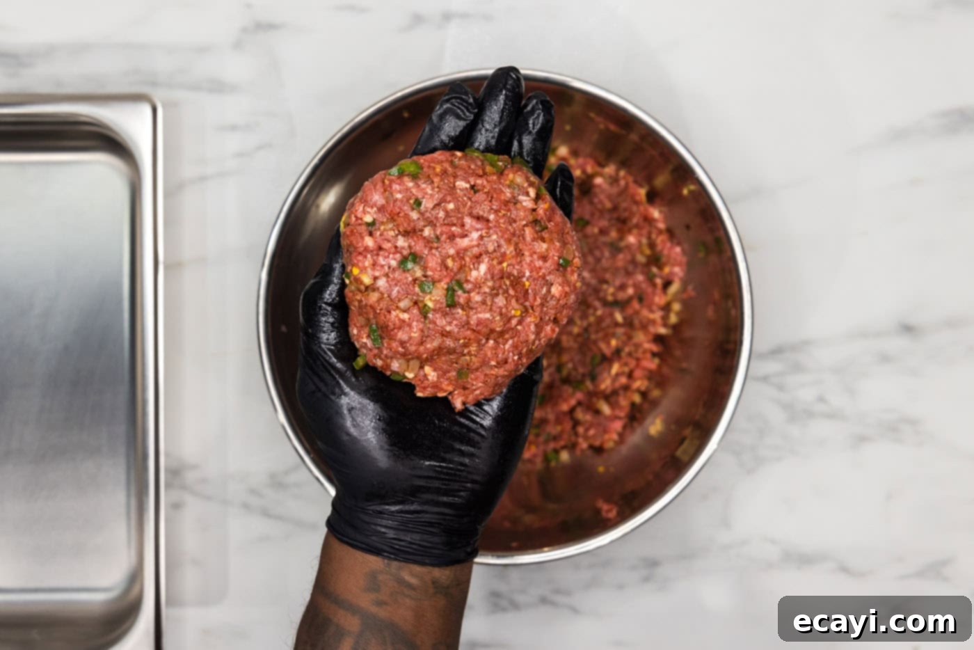 Taco Burger Fusion 7 A gloved hand gently shaping a burger patty with a thumb indentation in the center.