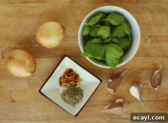 Optional fresh tomato sauce seasonings: onion, garlic, dried oregano, red pepper flakes, fresh basil // FoodNouveau.com A selection of fresh herbs and spices for enhancing tomato sauce, including a red onion, garlic cloves, dried oregano, red pepper flakes, and fresh basil leaves. These are key ingredients for any homemade fresh tomato sauce.