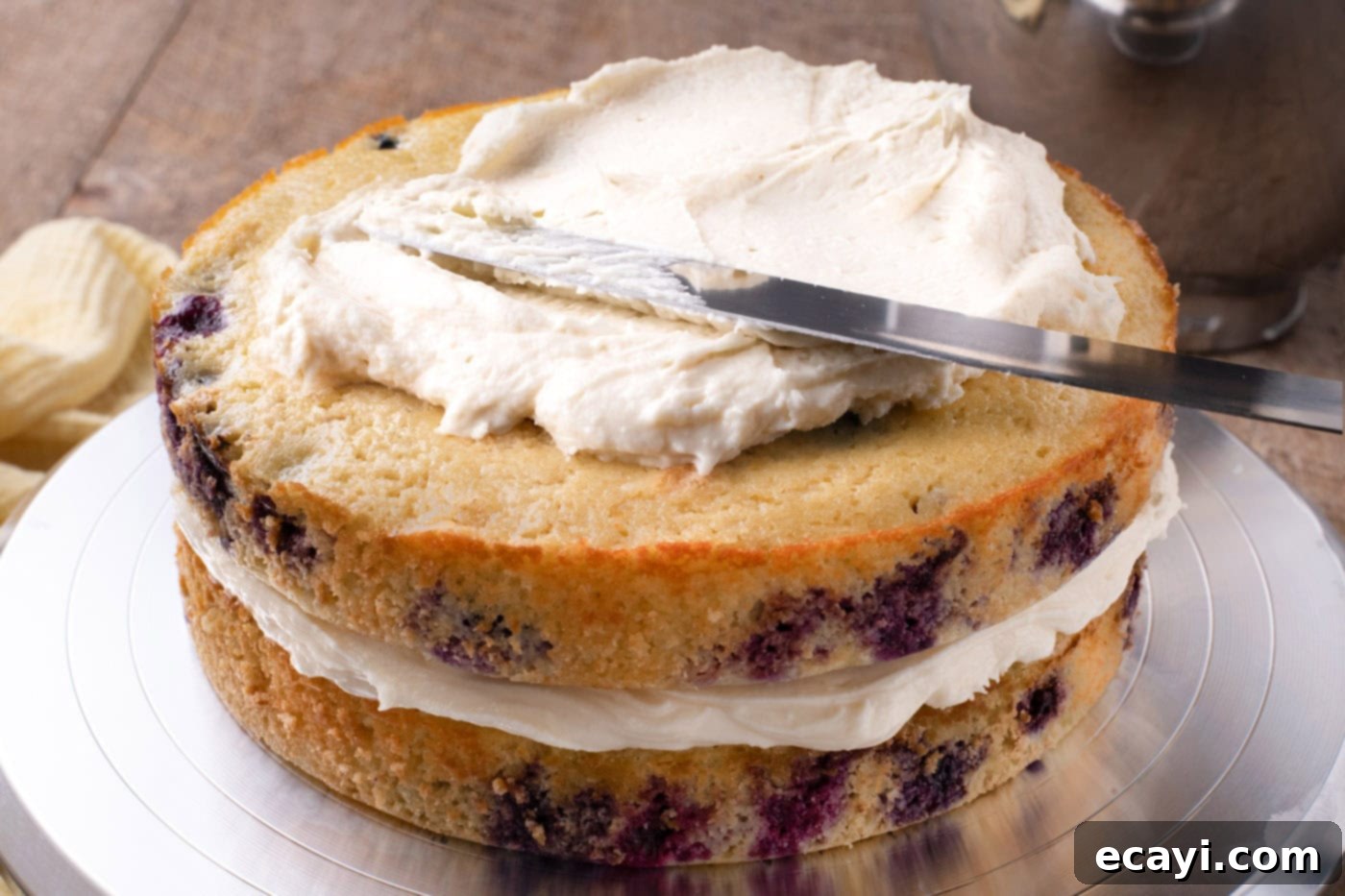 Zesty Lemon Blueberry Bliss 13 Spreading thick cream cheese frosting over a layer of lemon blueberry cake