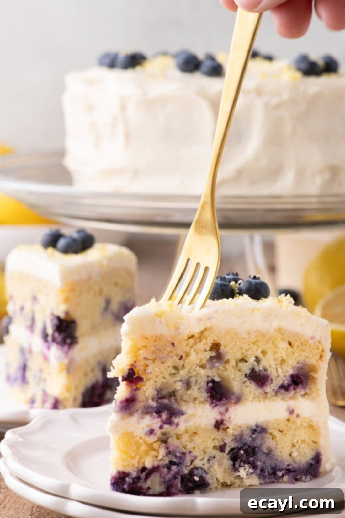 Zesty Lemon Blueberry Bliss 3 A fork taking a bite from a slice of Lemon Blueberry Cake with frosting and blueberries
