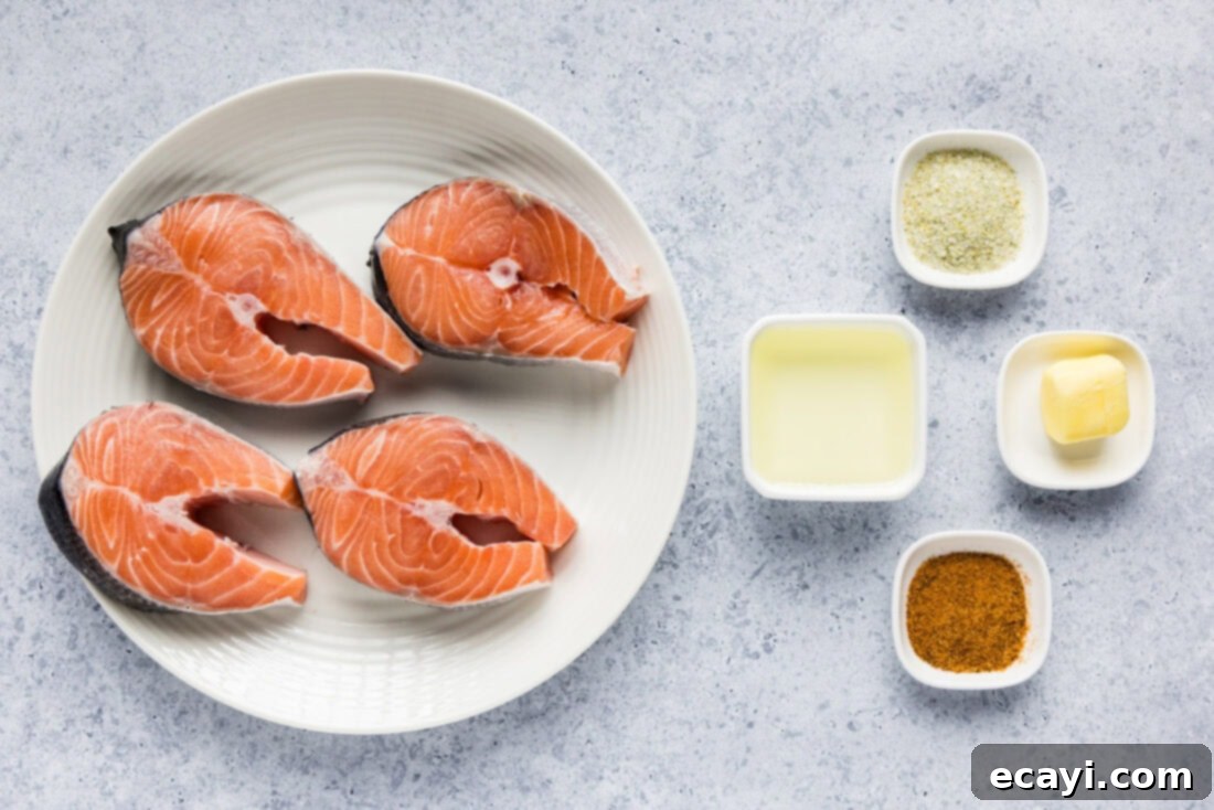The Art of Perfect Salmon Steaks 4 A collection of fresh ingredients for pan-seared salmon steaks, including raw salmon steaks, a block of butter, a bottle of olive oil, and small bowls of garlic salt and Old Bay seasoning, neatly arranged on a rustic wooden board.