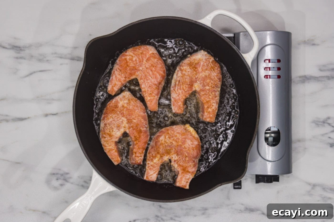 The Art of Perfect Salmon Steaks 6 Two salmon steaks actively cooking in a hot skillet, with a golden-brown crust forming on the underside. Lemon wedges are visible in the background.