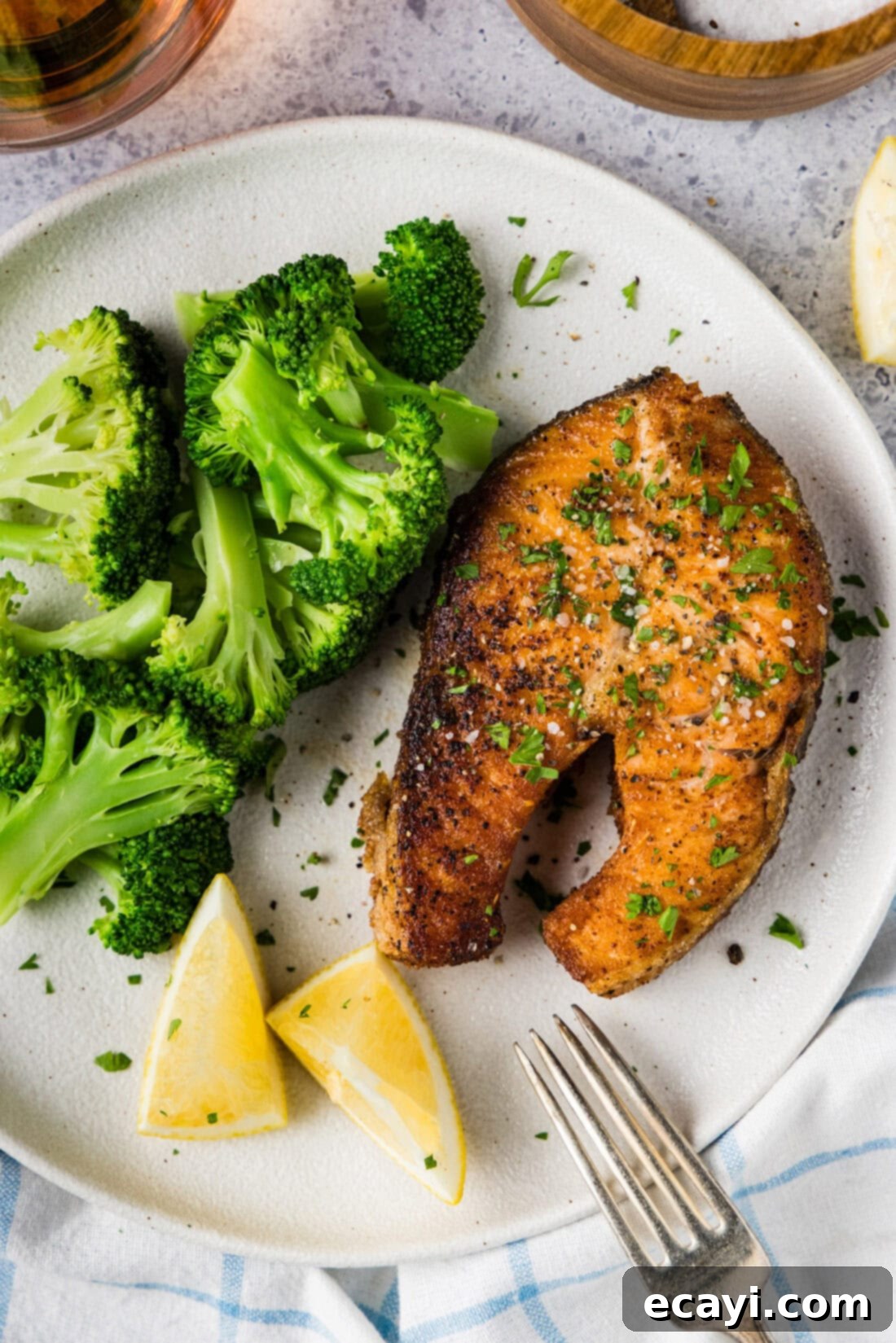 The Art of Perfect Salmon Steaks 7 A beautifully presented pan-seared salmon steak on a white dinner plate, accompanied by vibrant green roasted broccoli florets and fresh lemon slices. A sprinkle of fresh dill garnishes the fish.