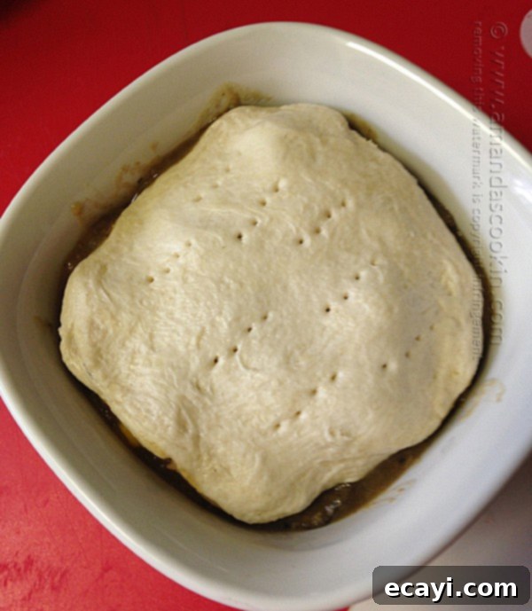 Homestyle Beef Biscuit Pot Pie 9 A close-up view of a flattened, fork-pricked biscuit carefully placed on top of a portion of beef stew in an individual ramekin, ready for baking.