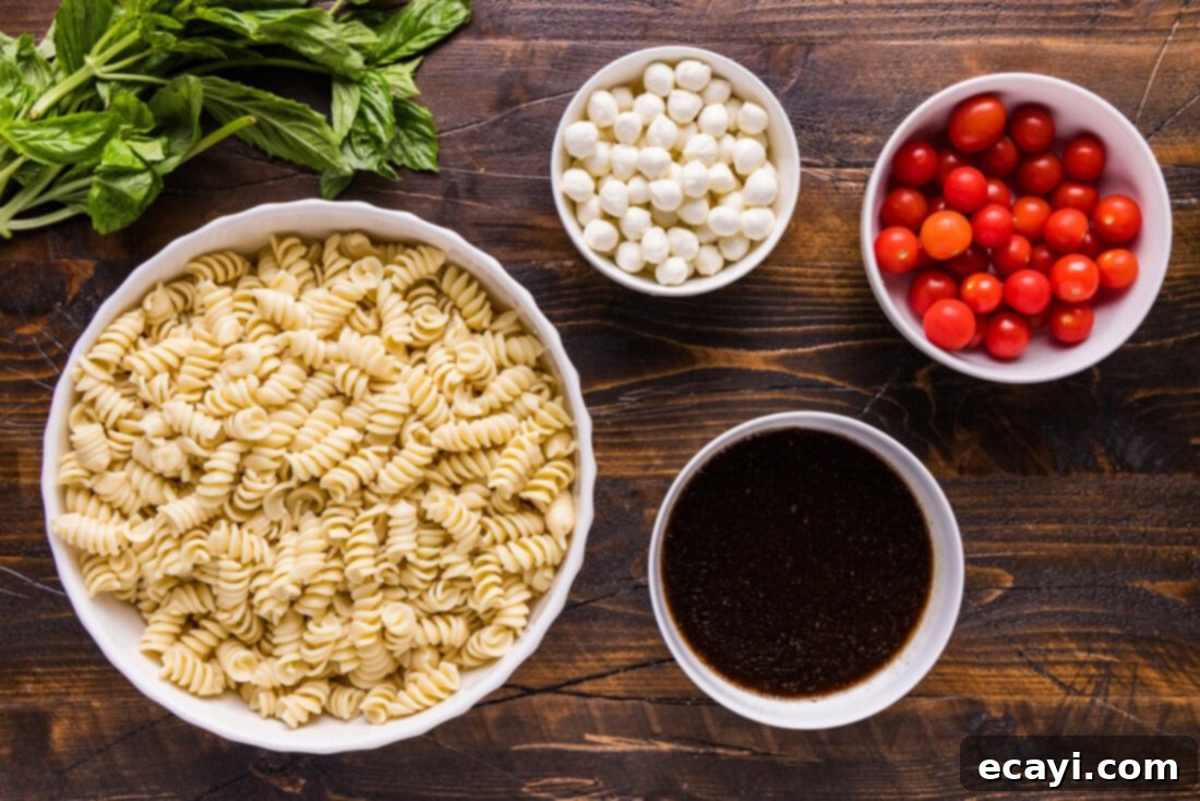 Caprese Pasta Delight 4 Fresh ingredients laid out for making Caprese Pasta Salad, including rotini, cherry tomatoes, mozzarella, and basil.