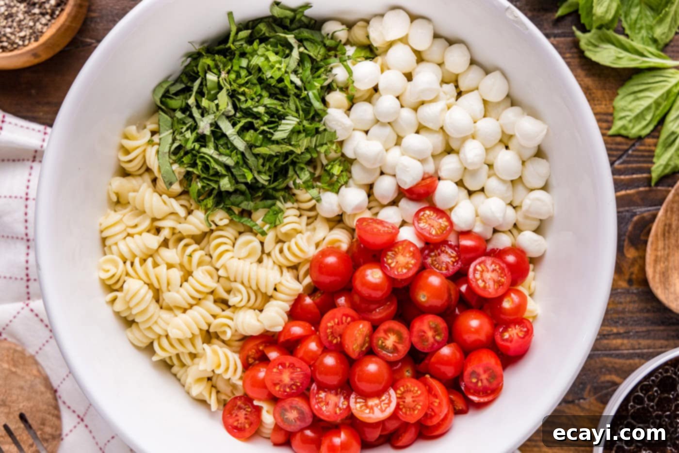 Caprese Pasta Delight 5 Chopped basil leaves, halved cherry tomatoes, mozzarella balls, and cooked pasta in a large mixing bowl, ready for dressing.