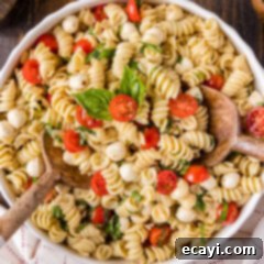Caprese Pasta Delight 8 Close up photo of Caprese Pasta Salad in a bowl with two spoons, highlighting the fresh mozzarella, tomatoes, and basil.