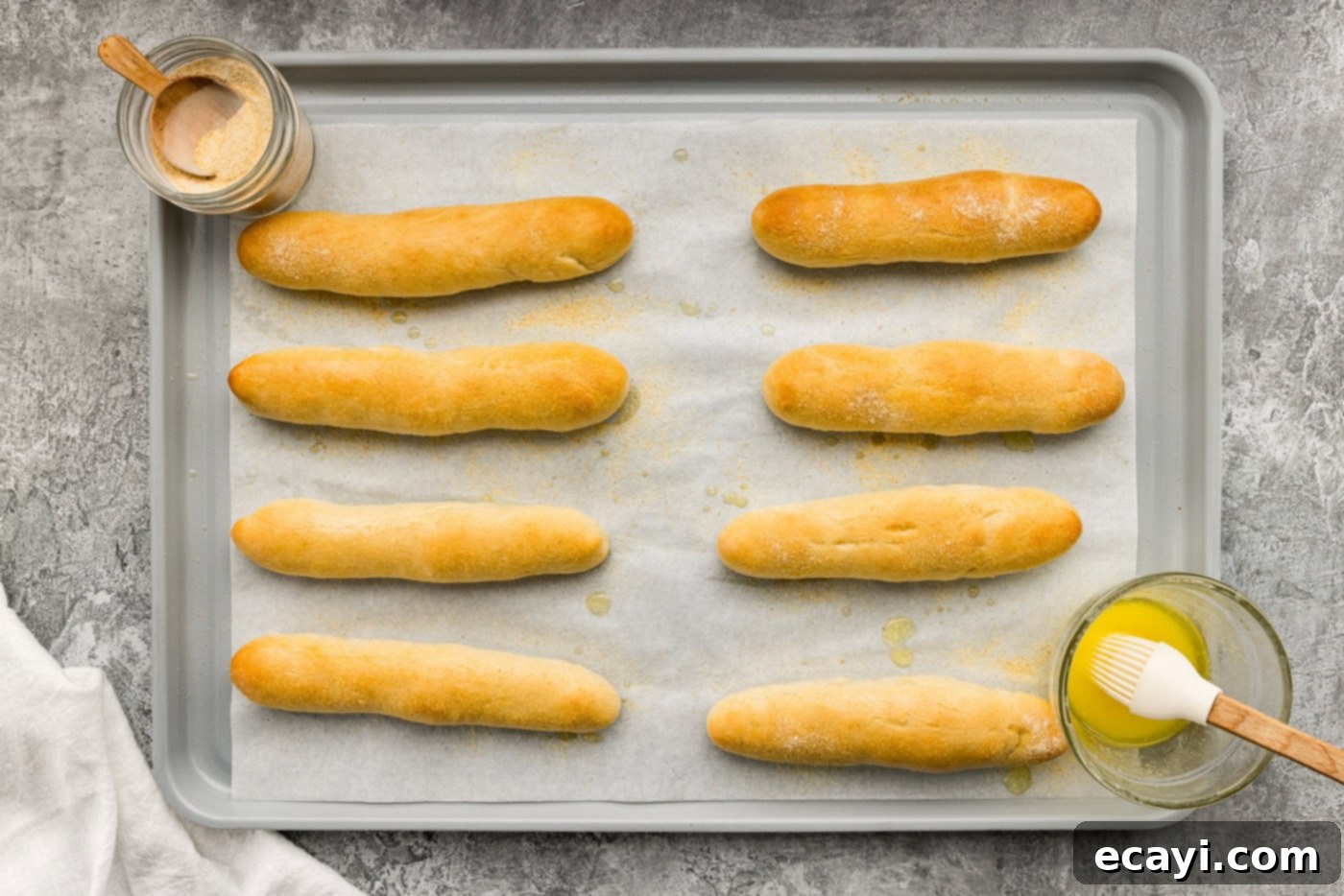 Endless Warm Garlic Breadsticks 14 Overhead view of freshly baked breadsticks on a baking sheet, being brushed with melted butter and sprinkled with garlic salt.