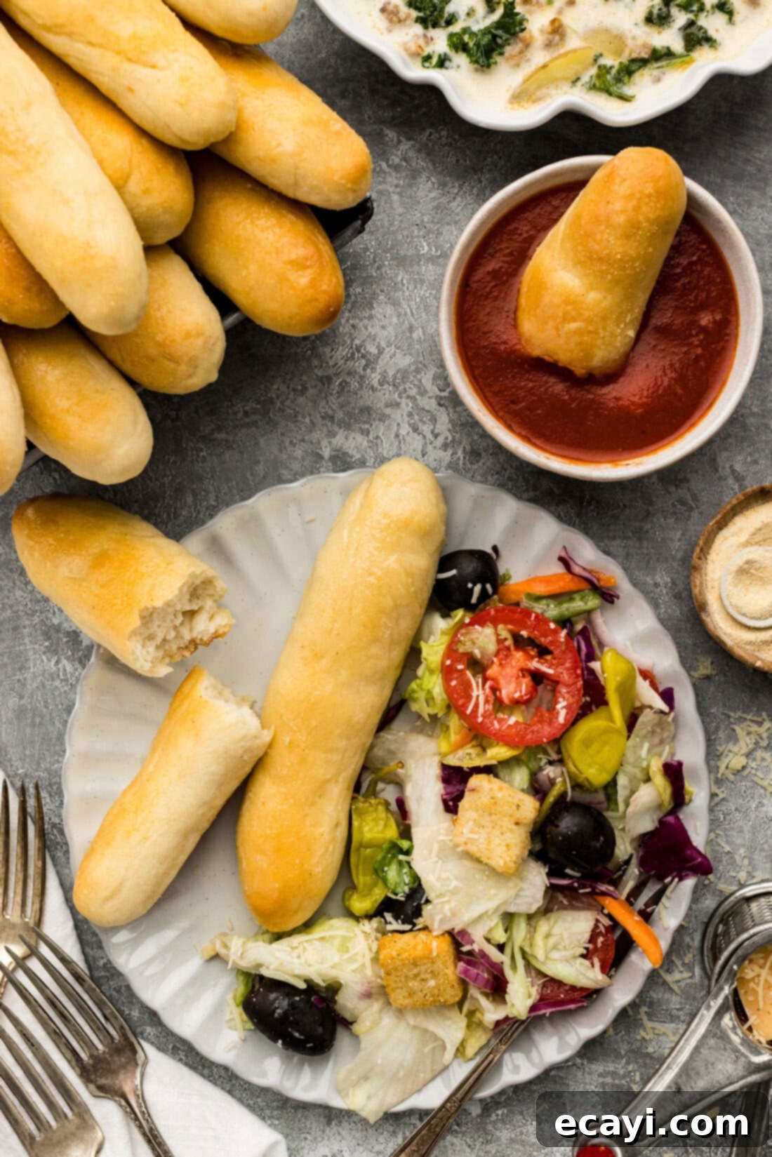 Endless Warm Garlic Breadsticks 3 A perfectly baked Olive Garden style breadstick, broken in half, resting on a plate next to a fresh garden salad.