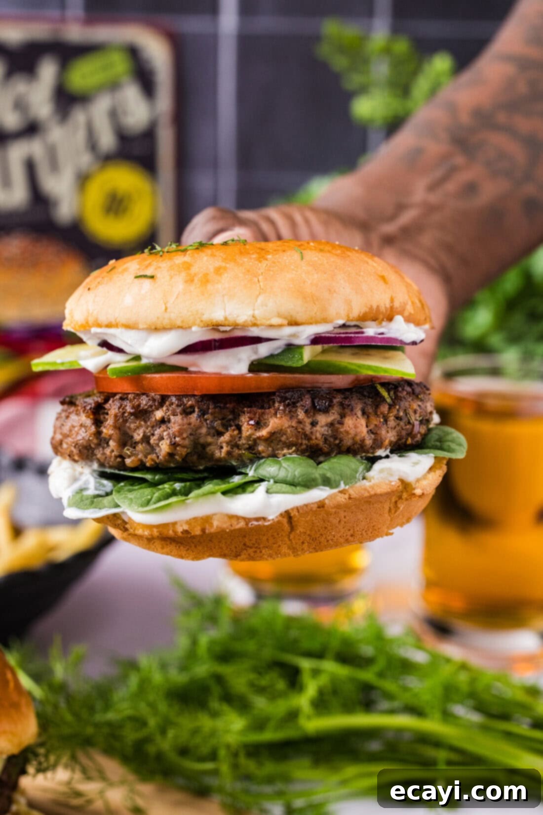 Crafted Lamb Burgers 2 Hand holding a Lamb Burger garnished with fresh greens and a creamy sauce