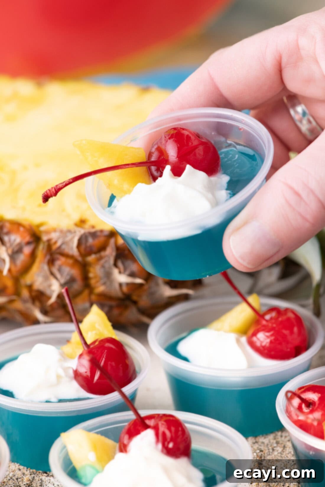 Blue Lagoon Jello Shooters 3 A hand holding up a single Blue Hawaiian Jello Shot, showcasing its bright blue color and tropical garnish.