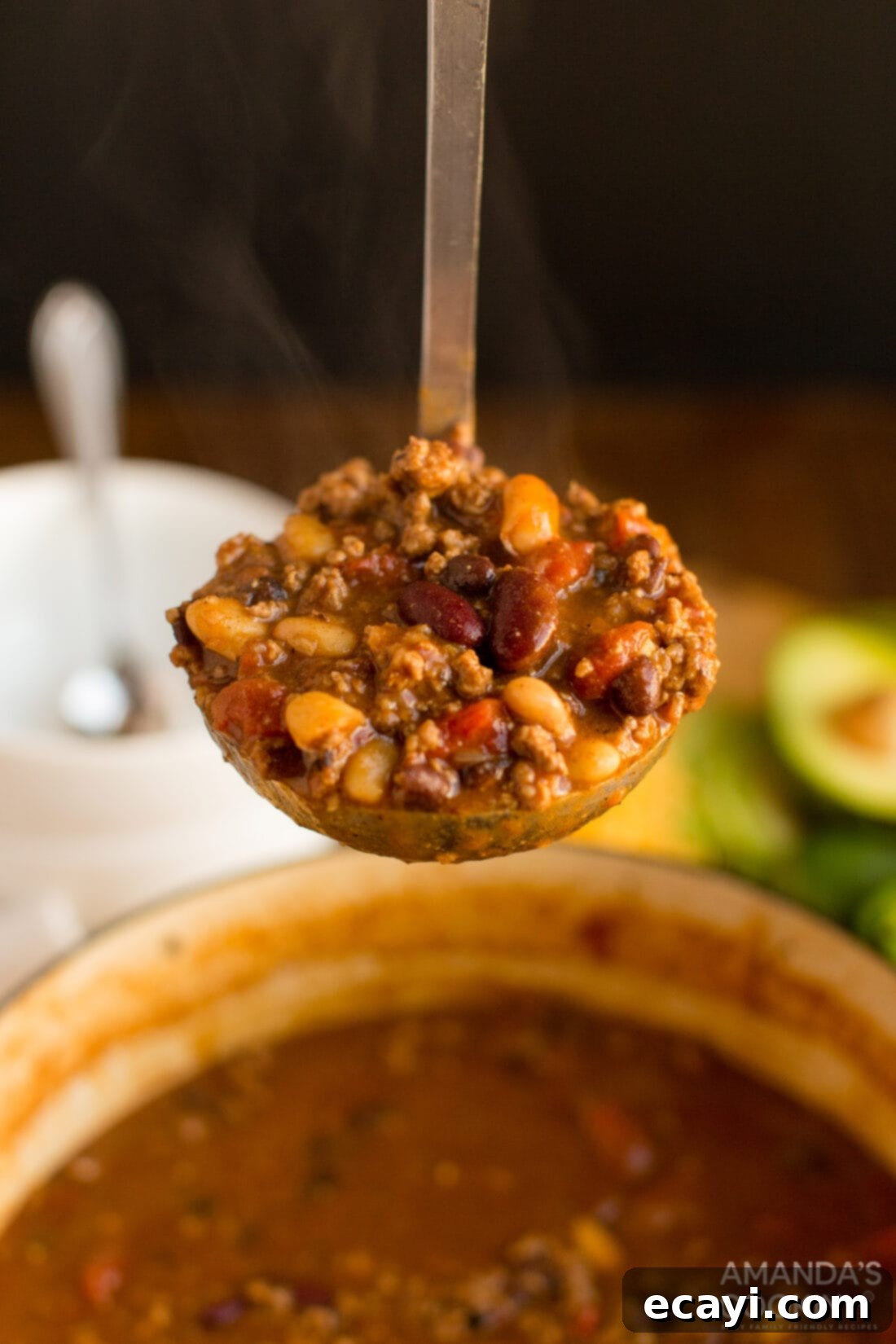 This 3 Bean Chili is made with a homemade chili seasoning, fresh ground beef, fire roasted tomatoes, and three types of canned beans. Great for football!  A ladle full of hearty 3 Bean Chili, showcasing rich colors and textures, ready to be served into a bowl.