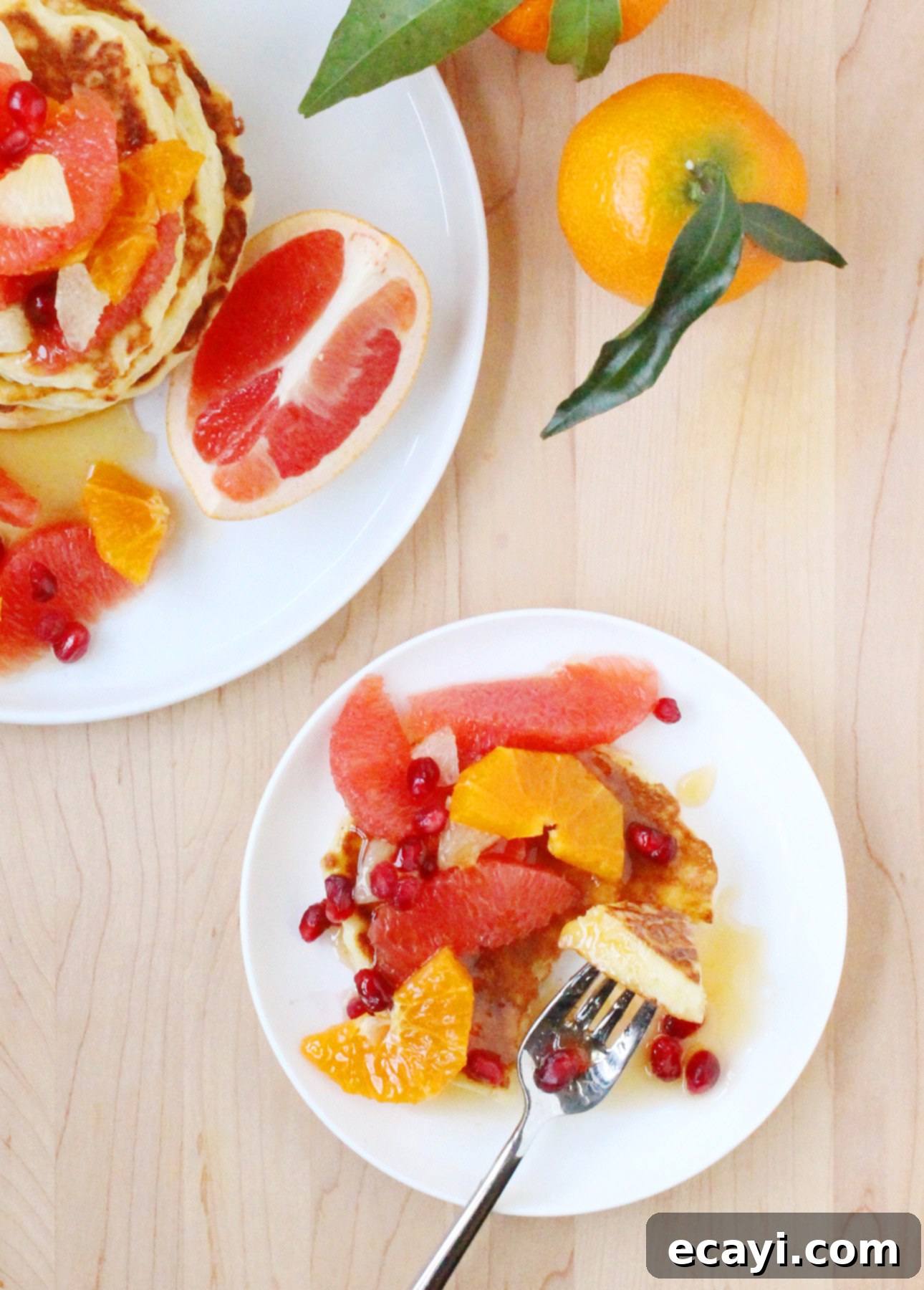 Zesty Ricotta Pancakes with Golden Citrus Drizzle 5 A high stack of Citrus Ricotta Pancakes on a white plate, adorned with fresh citrus fruits and drizzled with golden syrup.