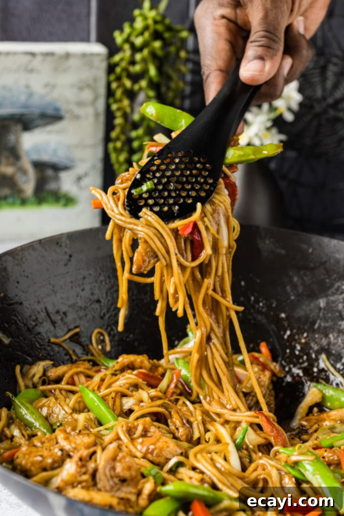 Classic Chicken Lo Mein 11 Tongs lifting a generous portion of Chicken Lo Mein, showcasing the long noodles, chicken, and colorful vegetables, from a wok.