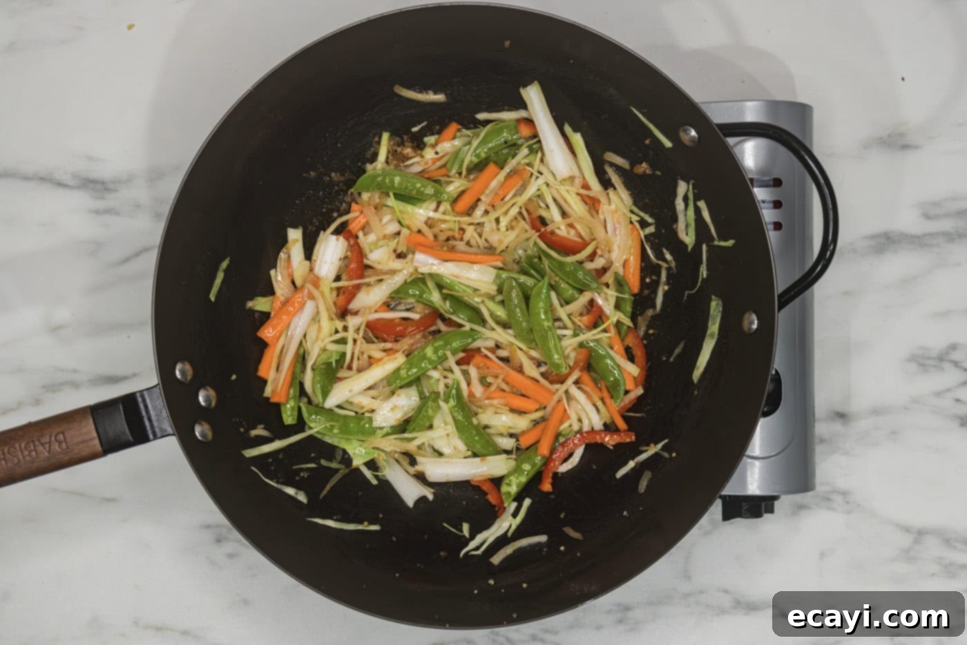 Classic Chicken Lo Mein 7 stir-frying a colorful array of chopped vegetables including garlic, ginger, onion, cabbage, bell pepper, snap peas, and carrots in a wok