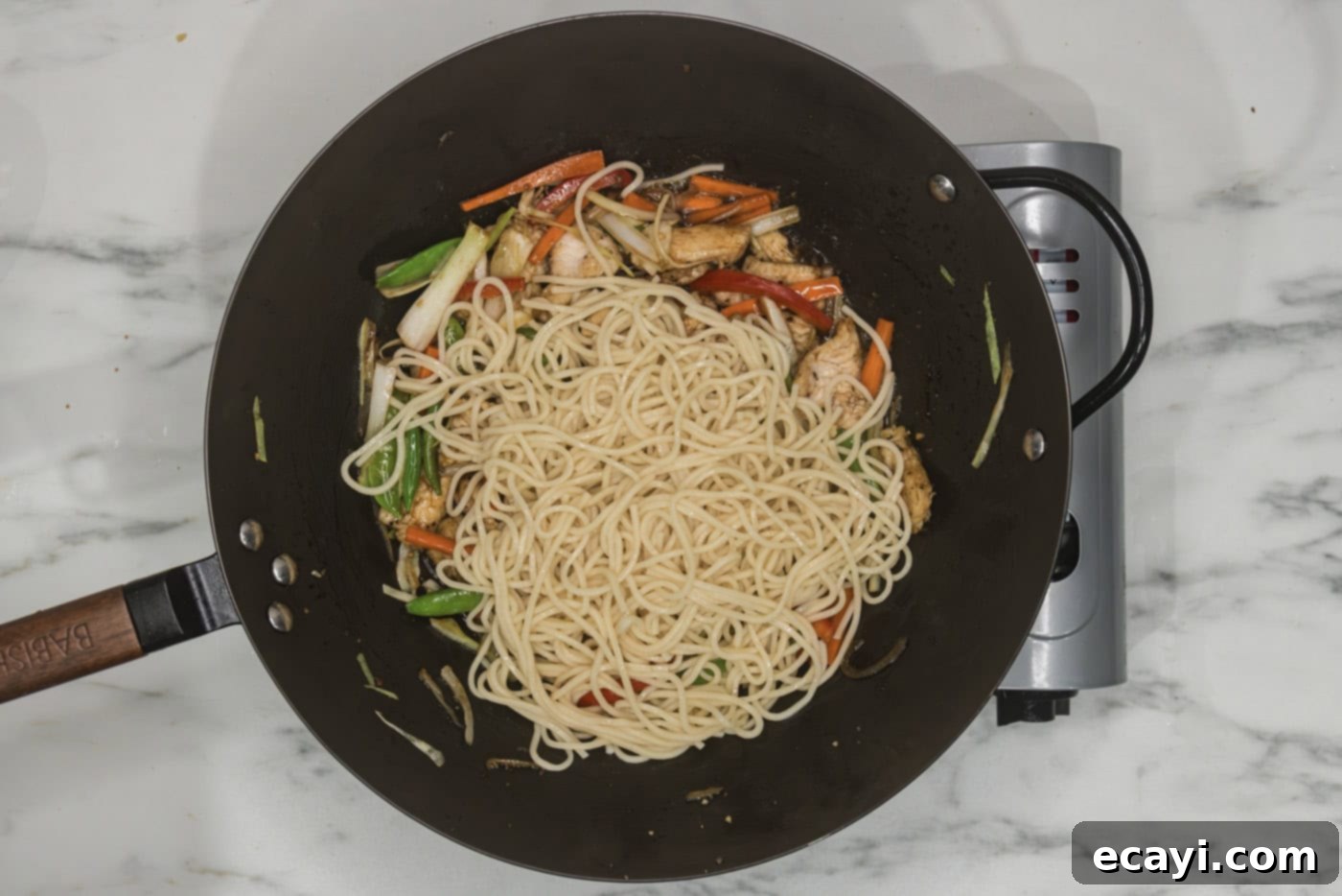 Classic Chicken Lo Mein 10 cooked lo mein noodles added to a skillet with sauced chicken and vegetables, being tossed together