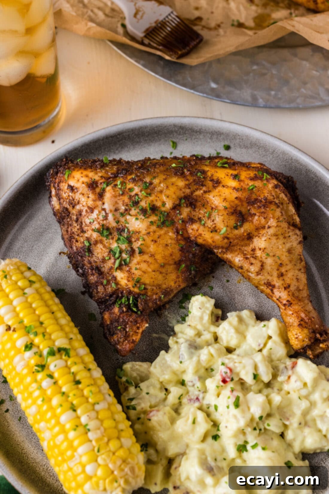 Juicy Smoked Chicken Quarters 3 Close up photo of a Smoked Chicken Quarter on a plate with potato salad and corn on the cob