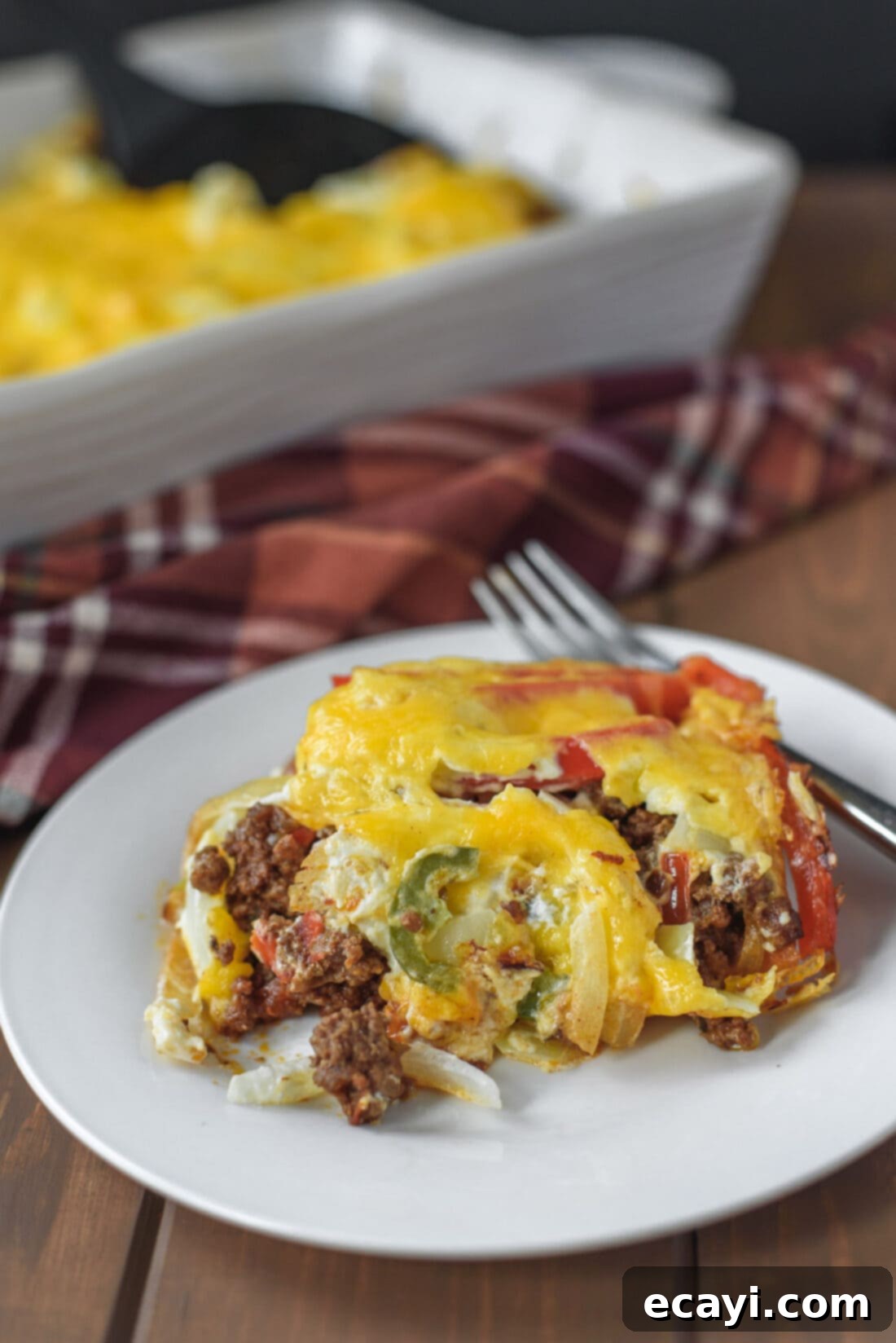 John Wayne Casserole: A savory beef, cheese, and biscuit bake that's perfect for dinner. Delicious and easy to make! A close-up shot of a single serving of John Wayne Casserole on a plate, topped with melted cheese and fresh vegetables.