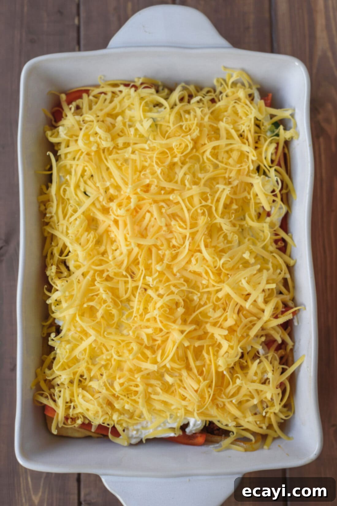 John Wayne Casserole topped with shredded cheese, ready to be baked to golden perfection! John Wayne Casserole in a baking dish, fully assembled and topped with shredded cheese, ready for the oven.